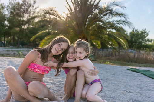 Portrait of three cute girls in swimsuits looking at camera while sitting at the beach