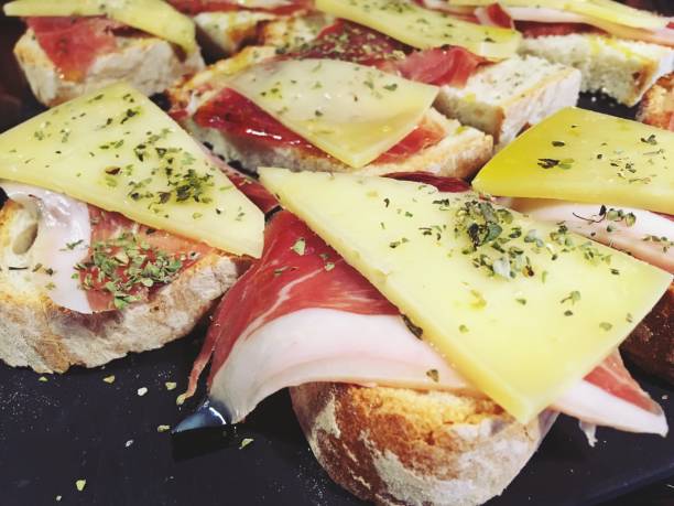Tapa of Serrano ham and cheese with olive oil and oregano on a slice of bread. Tapas on display at the bar of a restaurant in Madrid to accompany the drink for free. Spain. machego stock pictures, royalty-free photos & images