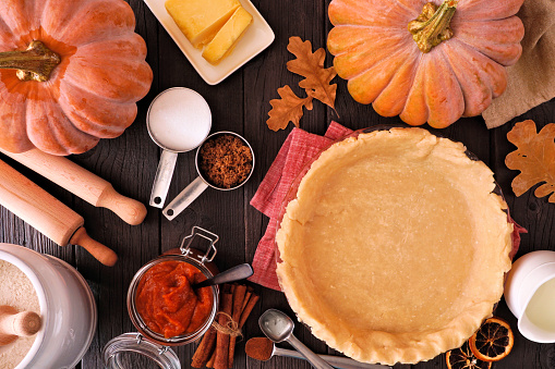 Autumn baking table scene with pumpkin pie ingredients. Overhead view on a dark wood background.