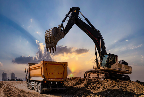 Crawler excavator during earthmoving works on construction site at sunset