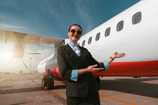 Woman stewardess standing near airplane and inviting on board. Blurred background