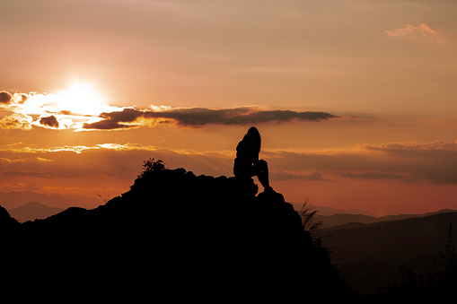 Woman in the mountains enjoying amazing sunset view. She is on the top of one rocky hill. Hiking and walking in the nature concept. Summer time.