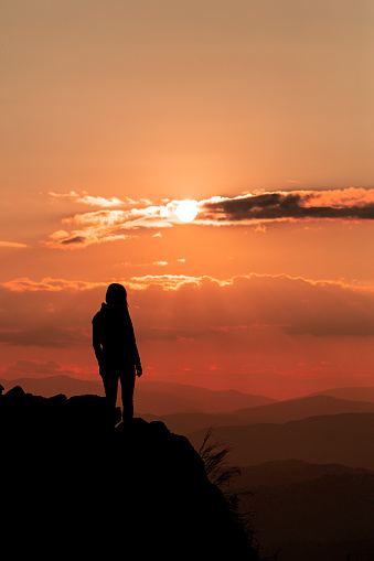 Woman in the mountains enjoying amazing sunset view. She is on the top of one rocky hill. Hiking and walking in the nature concept. Summer time.