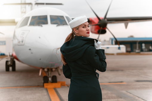 Back view of flight attendant standing near aircraft ready to flight. Blurred background