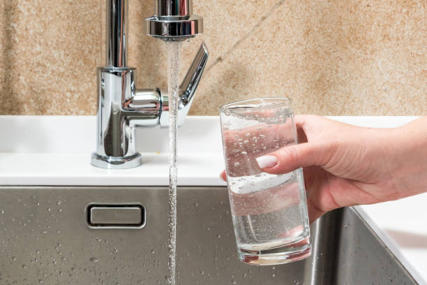 istock Water from a tap in a glass held by a woman's hand 1418820431