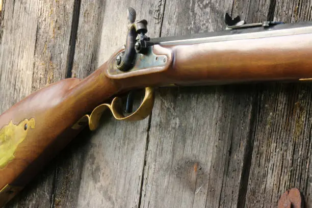 Photo of Close up of a Kentucky Black Powder Rifle percussion lock on an old plank background.