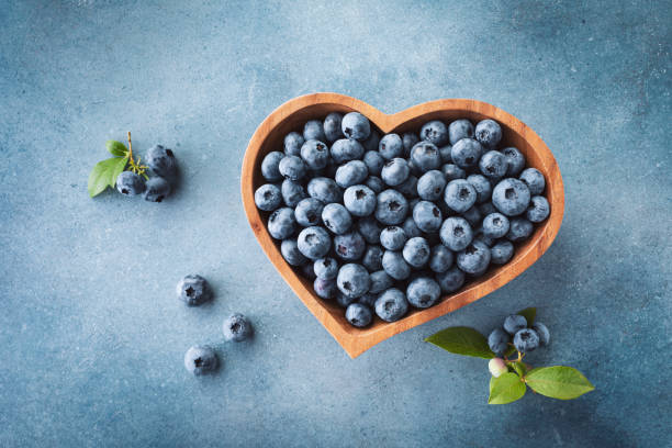 Heap of blueberry in bowl on blue table top view. Organic superfood and healthy berry. stock photo