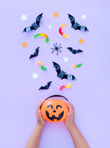 composition on the theme of the holiday Halloween a bucket of pumpkins in children's hands sweets bats spiders on a light background with a place for text