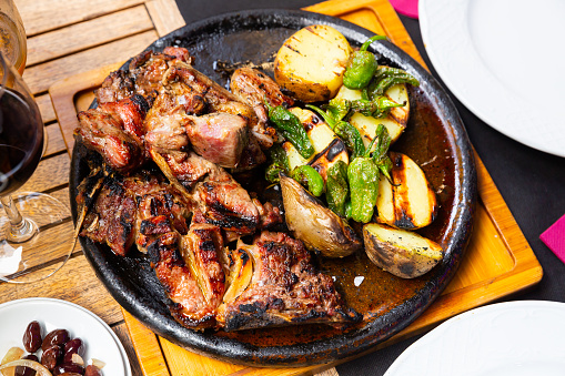Image of the popular Spanish dish Chuleton of beef steak with bone, served delicious potatoes and pepper in a frying 
pan