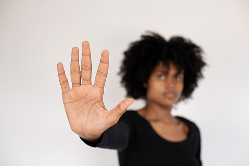 Close-up of palm of African American woman making stop gesture. Confident young woman wearing black T-shirt stretching arm for protection. Forbiddance and restriction concept
