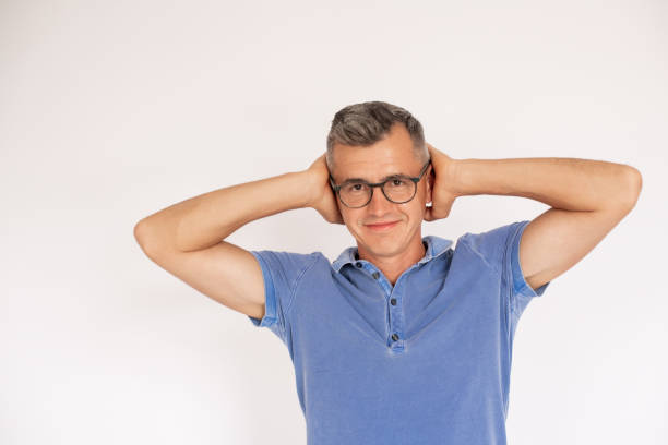 Portrait of happy mature man wearing glasses covering ears Portrait of happy mature man wearing glasses covering ears. Caucasian man wearing blue T-shirt looking at camera and smiling against white background. Noise concept man closing ears photos stock pictures, royalty-free photos & images