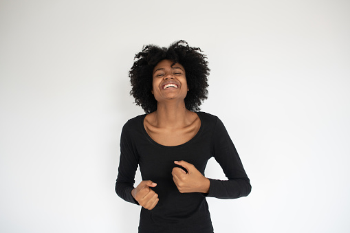 Portrait of laughing African American woman wearing black dress. Young female model looking at camera with joyful expression against white background. Happiness concept
