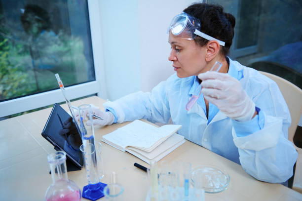 istock Multiethnic experienced woman, scientist pharmacist in white lab coat, writes down notes of her research in pharmacology 1418828061