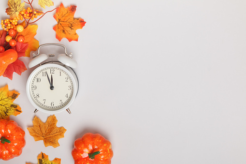 Alarm clock with fallen leaves, pumpkins. Transition change autumn time transformation, change of seasons. copy space
