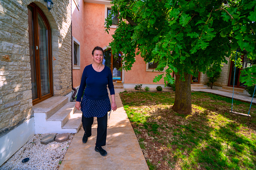 Mature woman doing morning exercising by walking around the tree in the vacation house backyard. She is in small place Peroj near Pula in Istria, Croatia with Brioni islands near by.