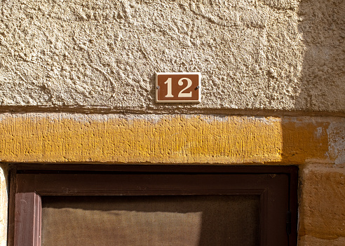 Street number twenty-five in the Southern France village of Alet-les-bains with white characters on a brown background, placed on a stone wall with some shadows
