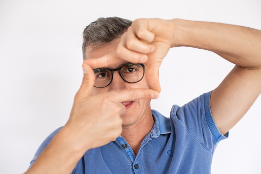 Man in glasses making frame with hands and fingers. Mid adult male model in T-shirt looking at camera. Creativity and photography concept.