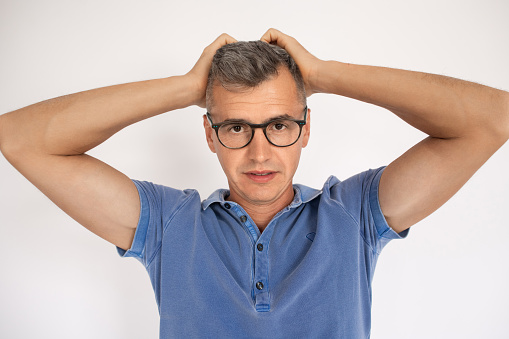 Portrait of striking man in glasses. Mid adult male model in T-shirt looking at camera, hands on head. Portrait, studio shot concept