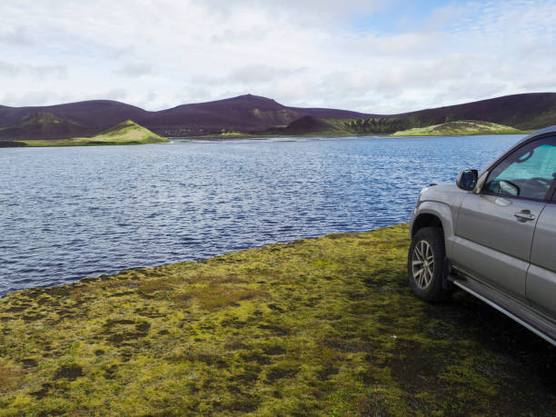 4x4 off road car standing on banks of blue crater lake and volcanic purple and green mountains in Veidivotn lakes, popular fishing area for local, central Iceland highlands in the middle of black lava desert. coche todoterreno 4x4 parado a orillas del lago del cráter azul y montañas volcánicas púrpura y verde en los lagos veidivotn, zona de pesca popular para las tierras altas locales del centro de islandia en medio del desierto de lava negra