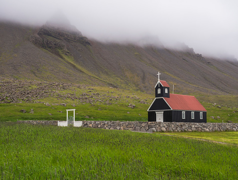 OLSaurbaejarkirkja black wooden red roof church on green grass field, steep hills in fog, Raudisandur, iceland west fjordsYMPUS DIGITAL CAMERA