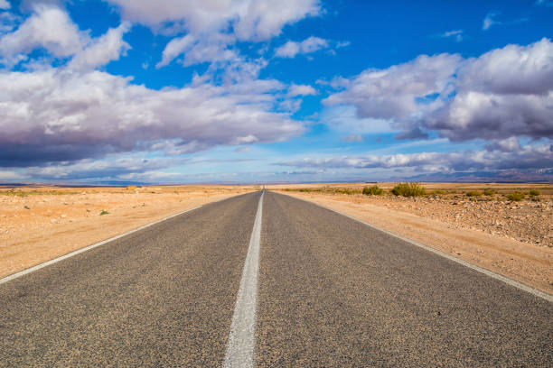 estrada interminável no deserto do saara sob belas nuvens em dia ensolarado. localização: deserto do saara, marrocos, áfrica. quadro artístico. mundo da beleza - arid climate asphalt barren blue - fotografias e filmes do acervo