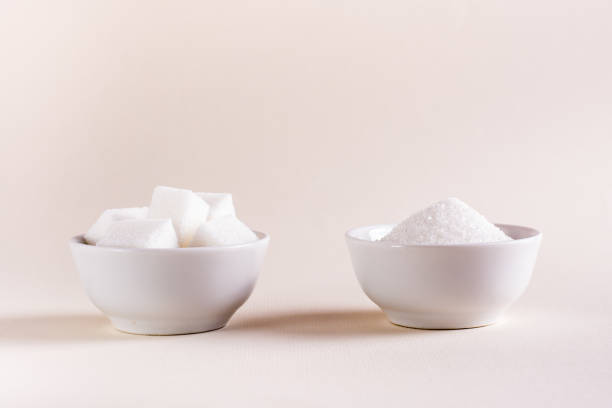 istock Sugar cubes and granulated sugar in bowls on a light background. Choosing between types of sugar 1418845672