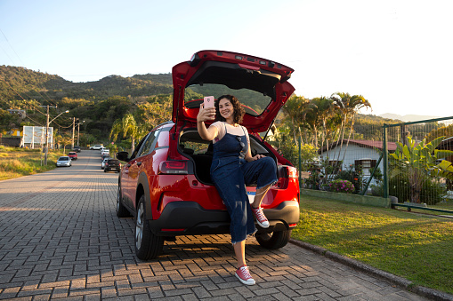 Latin woman doing selfie sitting in car trunk