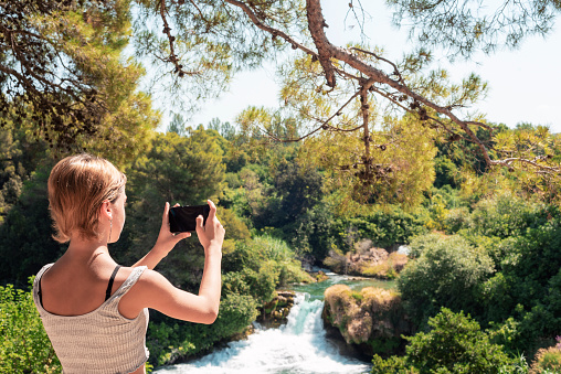 Beautiful teenage girl taking photo of waterfall. Krka waterfalls National park, Croatia.