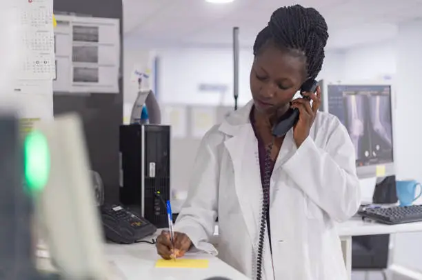 Young medical personel wearing a white lab coat speaking with a client or another doctor on the phone