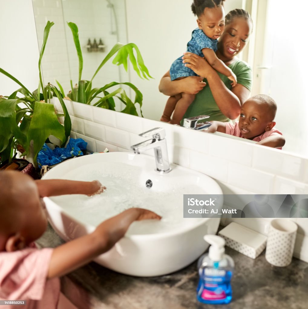 Mother carrying daughter looking at son washing hands in bathroom sink Reflection in bathroom mirror of mother carrying her daughter looking at her son washing hand in sink full of soap water Bathroom Stock Photo