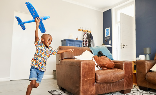 Cute little african boy holding a toy airplane and running in living room at home