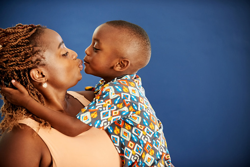 Side portrait of a loving african mother and son puckering for an affectionate kiss against blue background