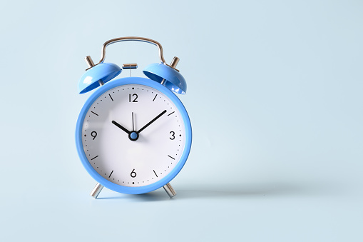 Old-fashioned blue alarm clock on blue background. Close up. Copy space.