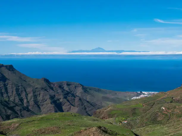 Photo of seascape view of cliffs and rocky atlantic coast in the north west of Gran Canaria with view on city of Puerto de las Nieves and Pico del Teide on Tenerife. Canary Islands, Spain.