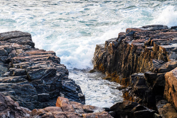 Dynamic scene of waves crashing against a rugged shoreline, capturing the essence of nature's power and beauty on a sunny day.
