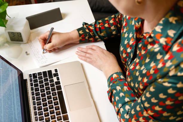 istock Defocus female hand writing pen. Unrecognizable elegant woman working on computer at office. Start or finish of a work day. Workspace. Top view. Time for work. Paperwork. Lifestyle. Out of focus 1418854818