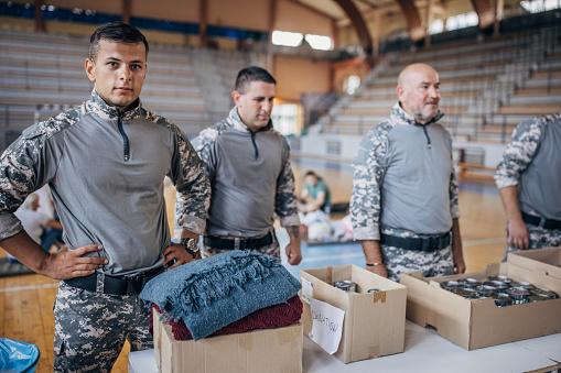 Group of people, soldiers on humanitarian aid preparing donations for civilians in school gymnasium, after natural disaster happened in city.