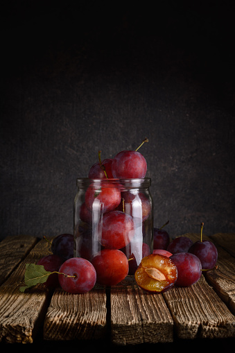 Whole and sliced red plums in a metal bowl on a dark gray background