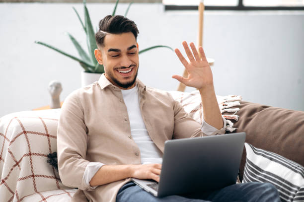 istock Online video communication. Glad friendly indian or arabian young man, freelancer or student, sitting on sofa at home in living room, talking on video conference with friend, colleague, client, smiles 1418863965
