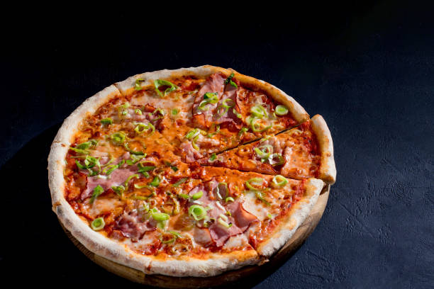 istock Delicious pizza with mozzarella cheese, ham, leeks on a tomato base on black background 1418863974