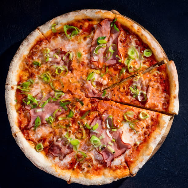 istock Delicious pizza with mozzarella cheese, ham, leeks on a tomato base on black background 1418863987