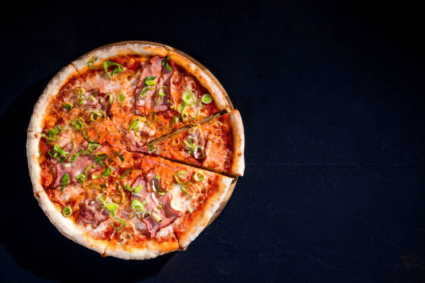 istock Delicious pizza with mozzarella cheese, ham, leeks on a tomato base on black background. Copy Space 1418863992
