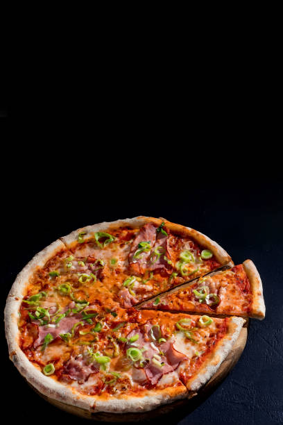 istock Delicious pizza with mozzarella cheese, ham, leeks on a tomato base on black background. Copy Space 1418864003