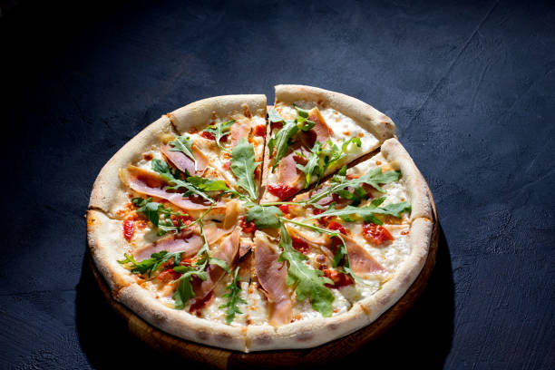 istock Pizza with jamon or prosciutto, mozzarella, cherry tomatoes, arugula and parmesan on a black background. Italian cuisine. 1418864042