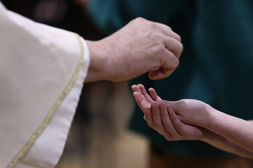 A priest about to place the  host bread or eucharistic wafer in to the hands of a parishioner at a mass liturgy or church ceremony. Serving communion