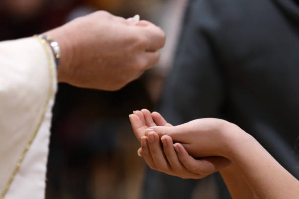 sacerdote in procinto di mettere l'ostia della comunione o il pane nelle mani di un parrocchiano - holy man immagine foto e immagini stock