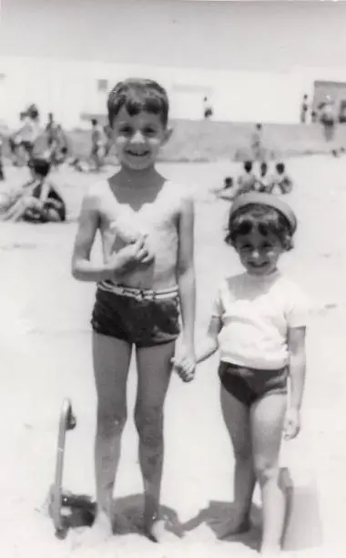 Vintage image from the sixties, a little boy and a little girl posing together smiling at the beach