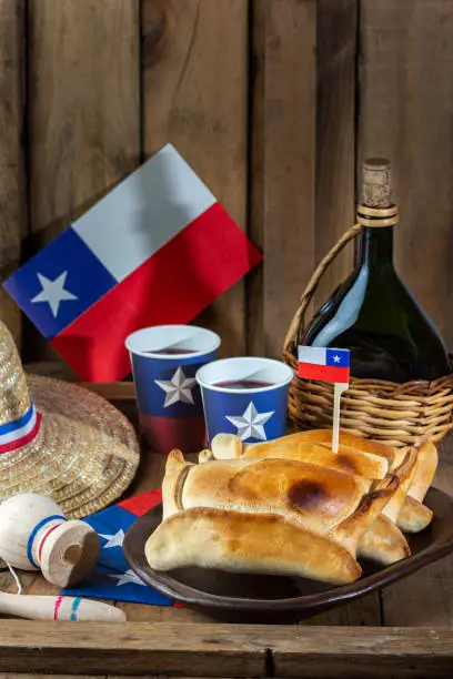 Photo of Chilean independence day concept. fiestas patrias. Tipical baked empanadas de pino, wine or chicha, hat and play emboque. Dish and drink on 18 September party, wooden background