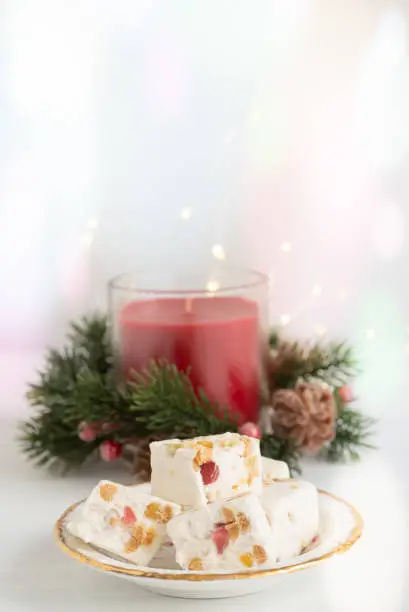 Nougat on Plate with Christmas Candle and Lights on Light Background with Copy Space Vertical
