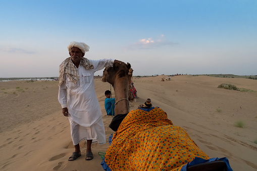 Thar desert, Rajasthan, India - 15th October 2019 : Two cameleers and their camels at sand dunes. Desert background. Cameleers make a living out of camel riding by tourists.